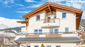 A multi-story building with a balcony, large windows, and a view of snow-covered mountains. - Apartment in Tyrol in an Attractive Area (Fiss)