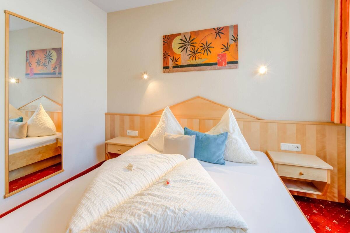 Une chambre d’hôtel avec un grand lit, une table de chevet, une commode, un miroir et un tableau au mur.