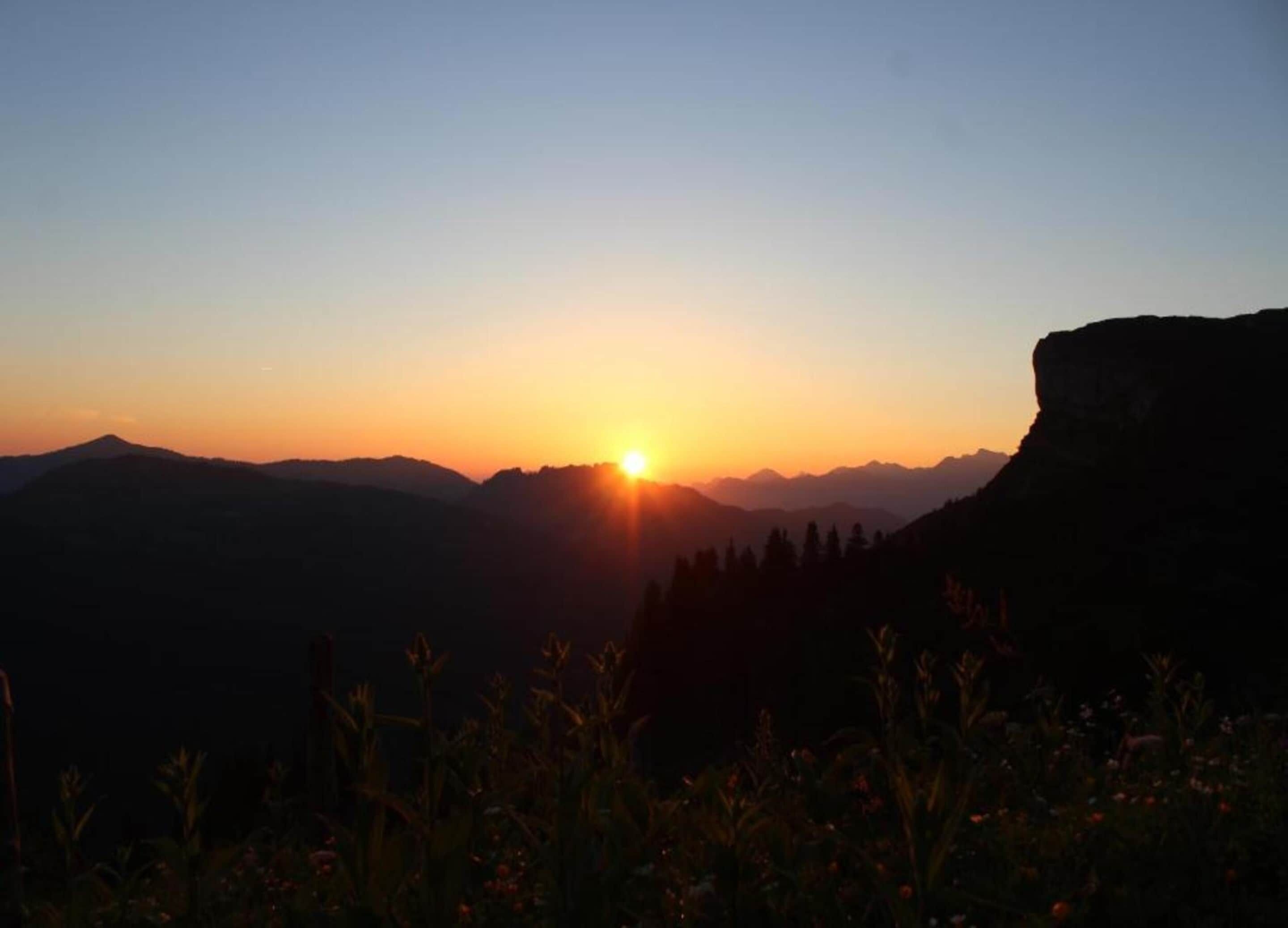 Un coucher de soleil sur un paysage montagneux, avec un ciel dégagé.