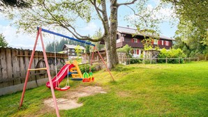 A playground with swings and a slide, surrounded by a wooden fence and a house in the background. - Chalet in Sibratsgfall Near Ski Slopes (Sibratsgfaell)