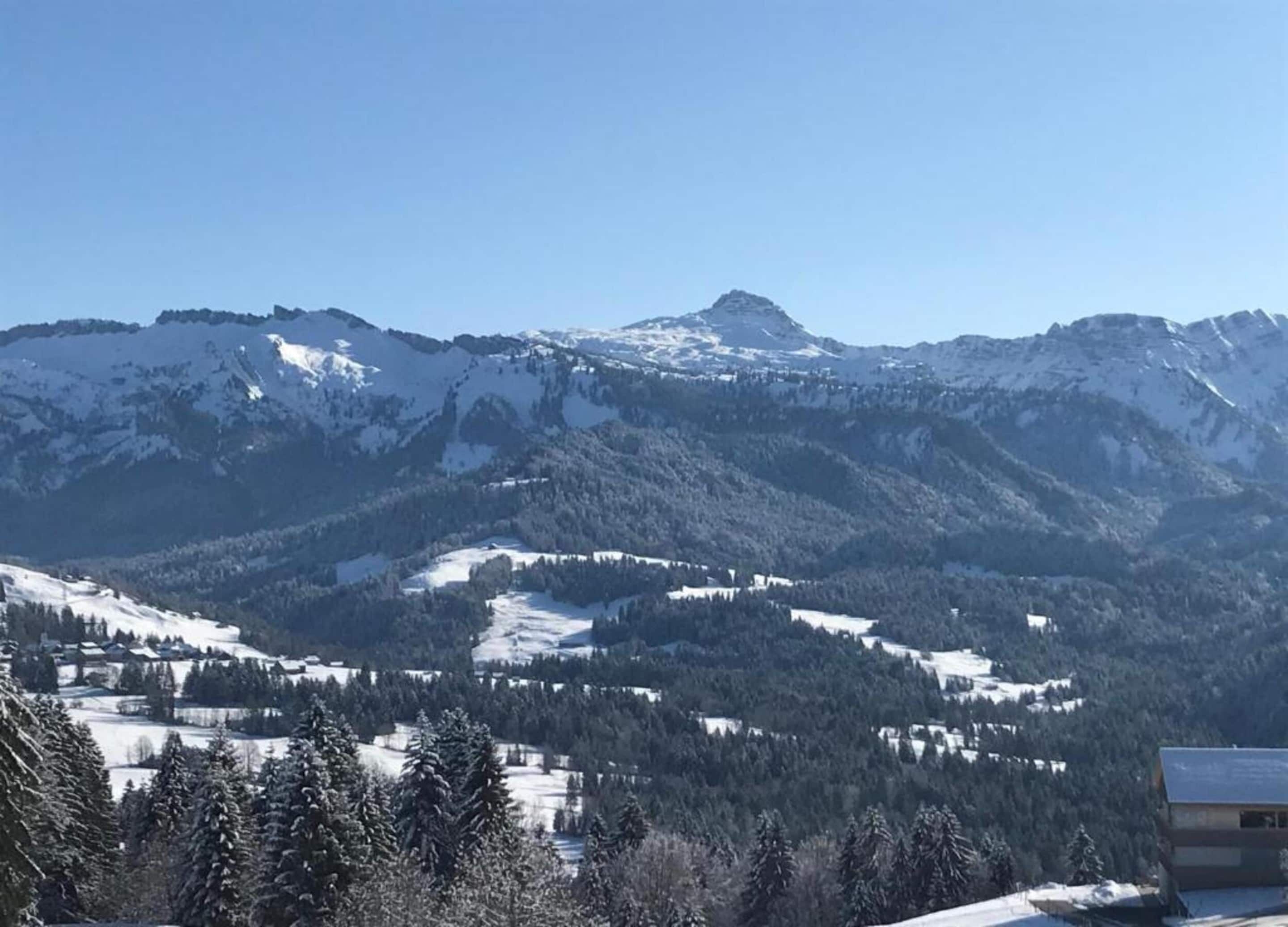 Un paisaje montañoso con picos nevados y un pequeño edificio en primer plano.