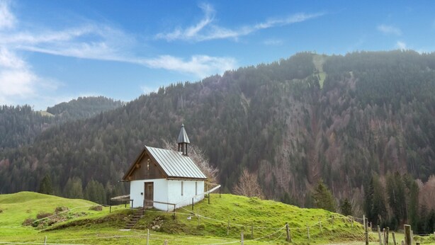 A small white church with a bell tower on a grassy hill, surrounded by forested mountains. - Chalet in Sibratsgfall Near Ski Slopes (Sibratsgfaell)