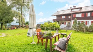 A grassy outdoor area with a wooden table and chairs, a white umbrella, and a sign. - Chalet in Sibratsgfall Near Ski Slopes (Sibratsgfaell)