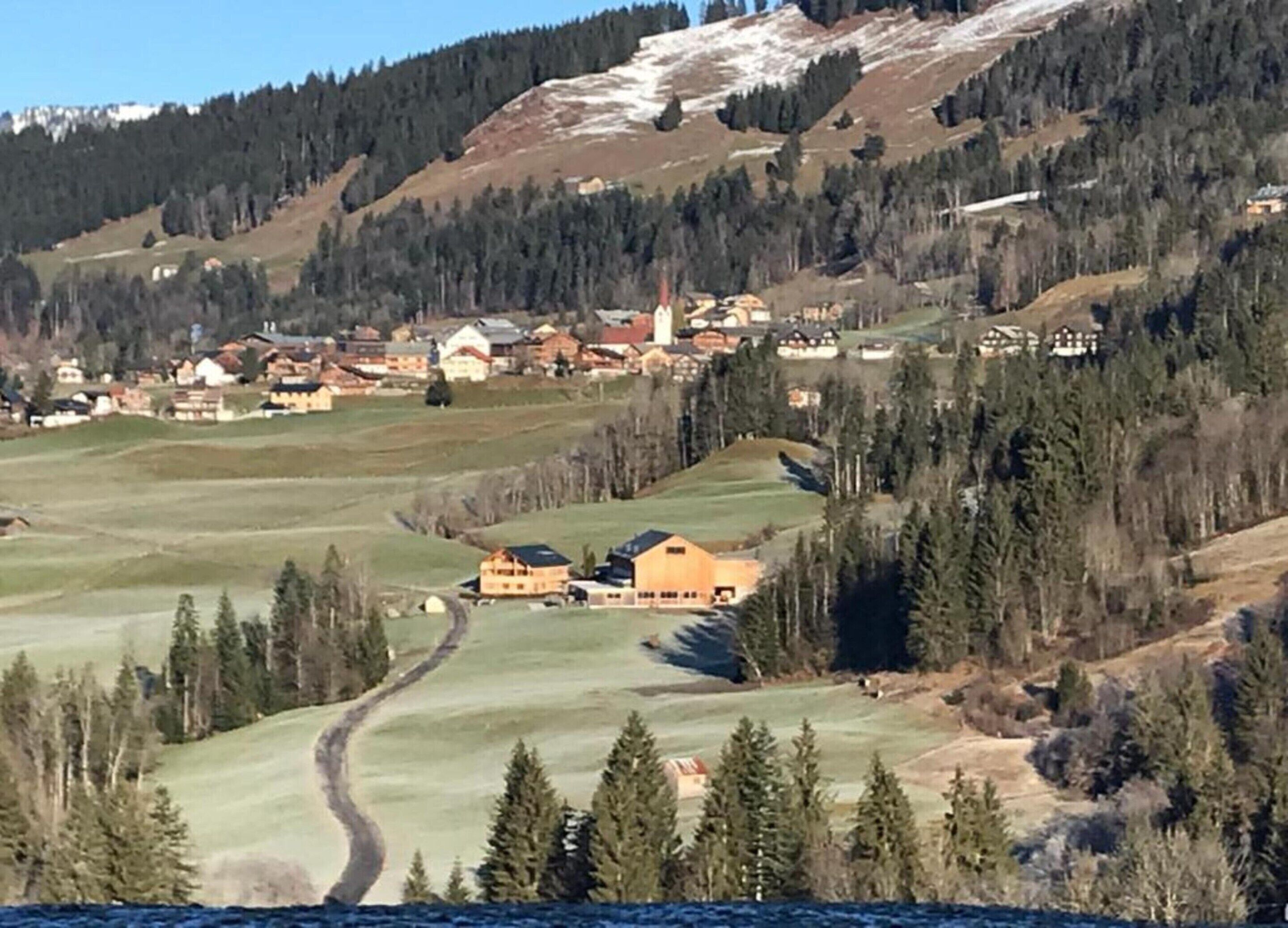Un pueblo rural con casas e iglesia, rodeado de bosques y colinas.