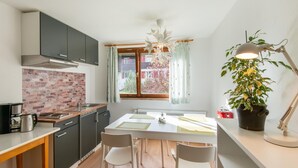 A modern kitchen with a brick backsplash, a dining table with chairs, a large window with curtains, and a potted plant. - Chalet in Sibratsgfall Near Ski Slopes (Sibratsgfaell)