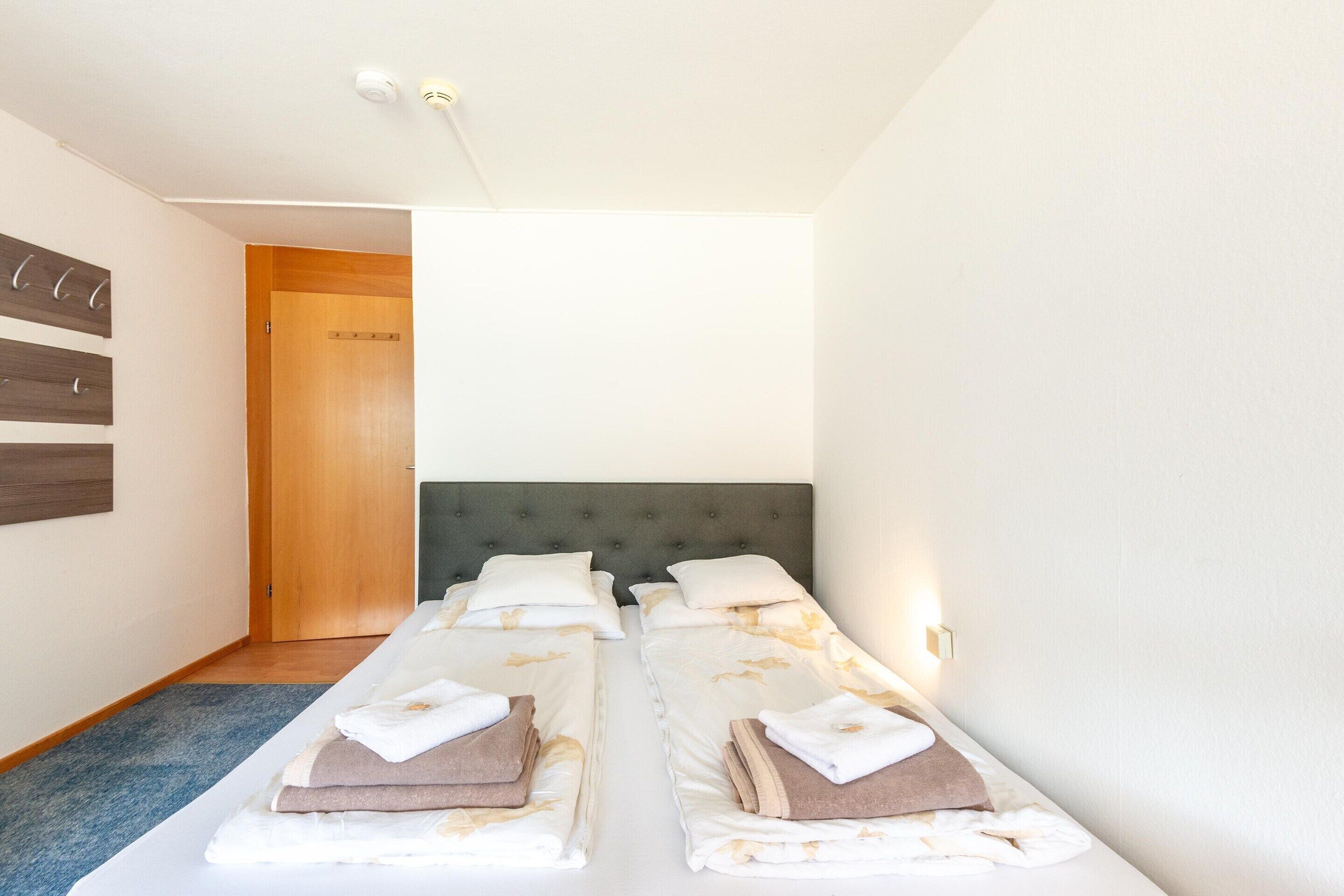Ein Hotelzimmer mit zwei Einzelbetten, einer Holztür, einem Lichtschalter und einem an der Wand befestigten Handtuchhalter.