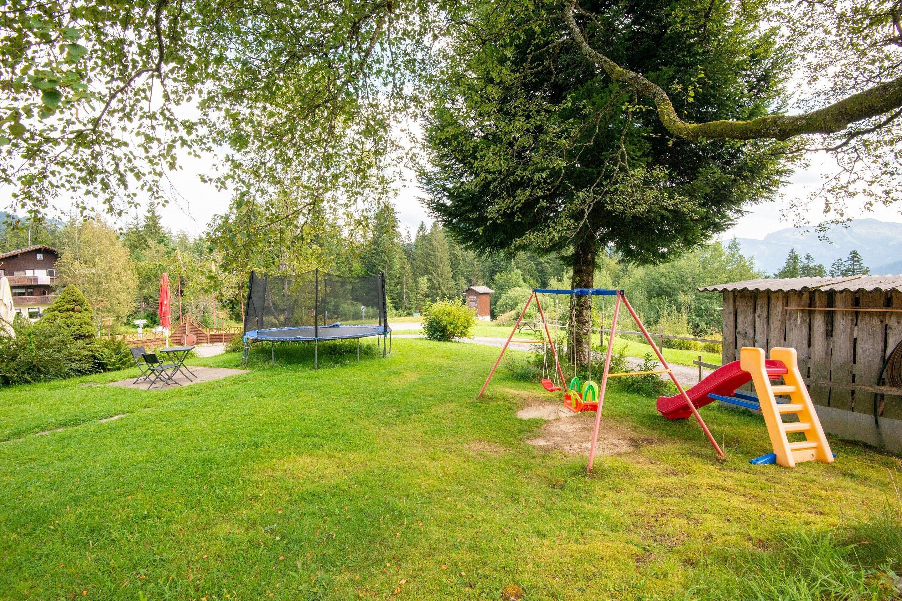 Ein Garten mit Rasen, Trampolin, Schaukel und Rutsche.