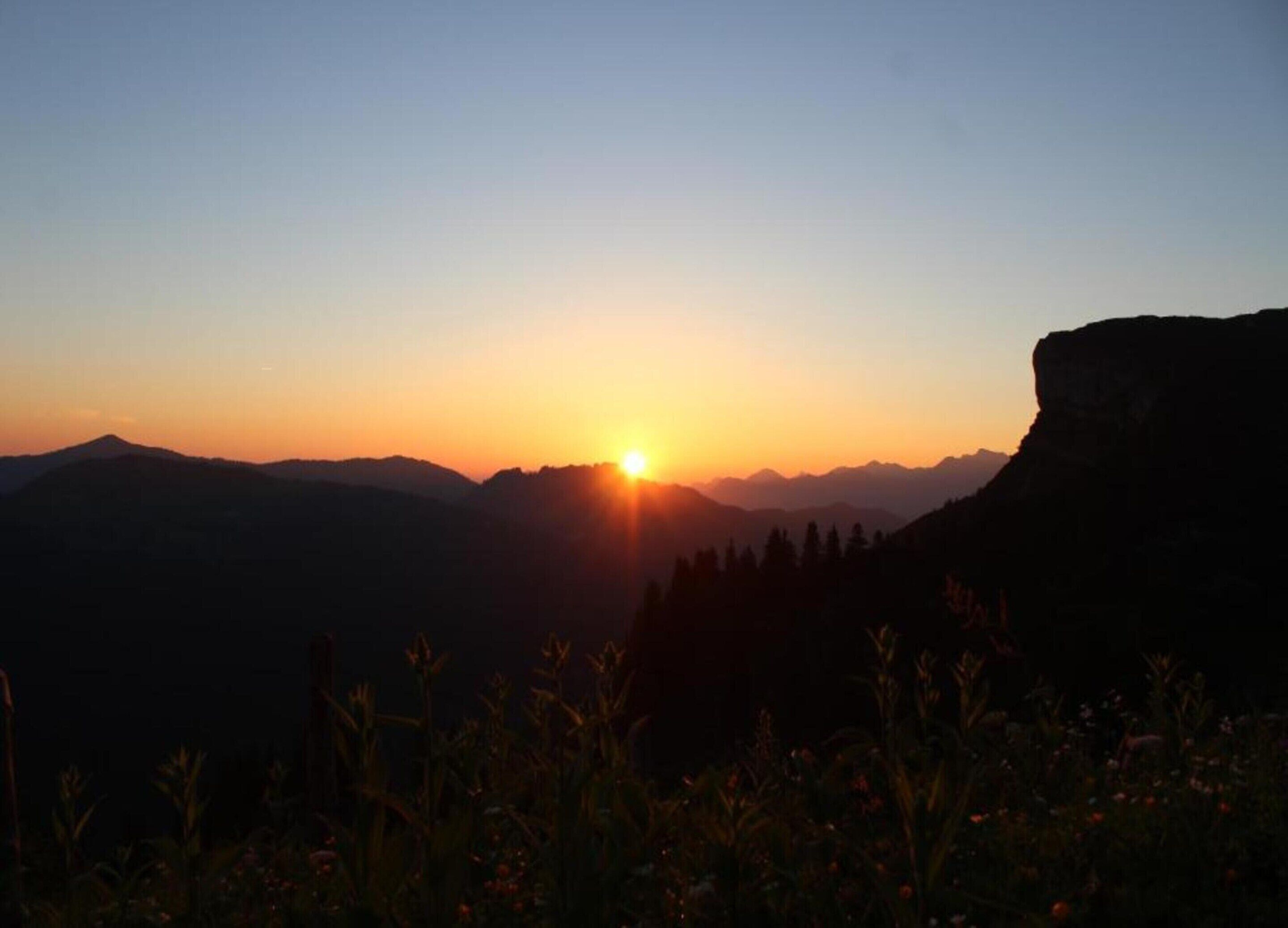 Ein Sonnenuntergang über einer Berglandschaft, mit einem markanten Felsen auf der rechten Seite.