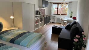 A bedroom with a bed, bedside lamp, wardrobe, kitchenette, and a seating area with a sofa and a table. - Chalet in Sibratsgfall Near Ski Slopes (Sibratsgfaell)