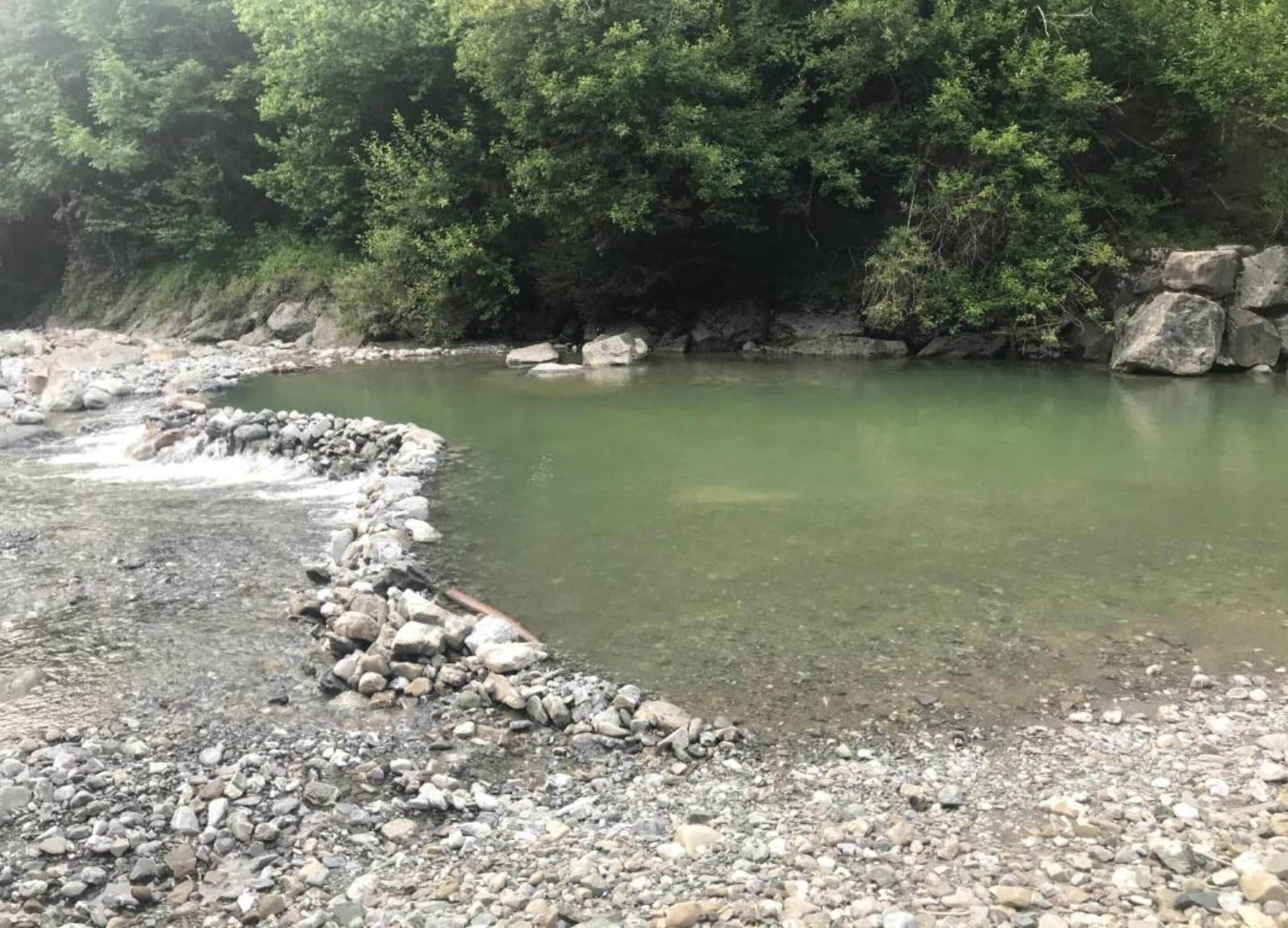 Un río de aguas transparentes, rodeado de rocas y un follaje verde denso.