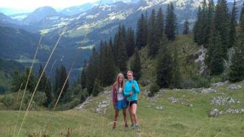 Dos personas en una colina cubierta de hierba, con un paisaje montañoso al fondo.
