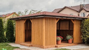 A wooden gazebo with a tiled roof, surrounded by a gravel path and potted plants.
