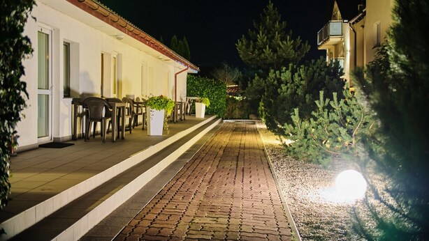 A paved pathway leading to a building with outdoor seating and potted plants.