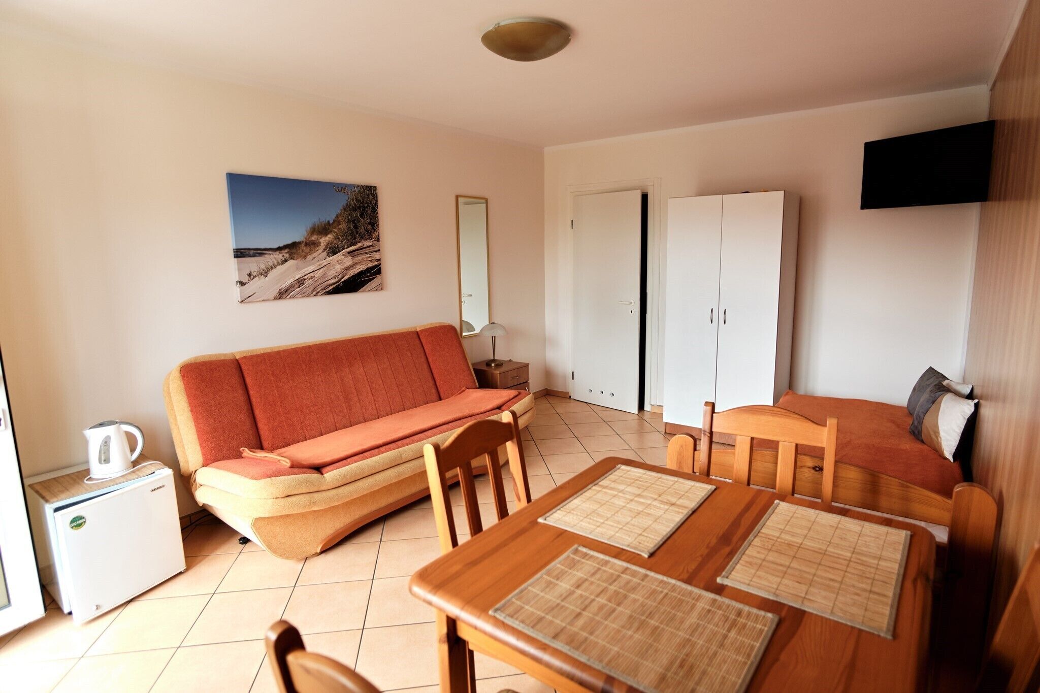A compact living space with a sofa, a small table, a cabinet, and a television mounted on the wall.