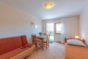 Une pièce de taille modeste comprenant un canapé, un lit, une table à manger avec des chaises et une fenêtre avec des rideaux.