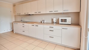 A modern kitchen with white cabinets, a wooden countertop, a sink, a kettle, and a microwave.