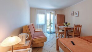 A compact hotel room with a sofa, a small table with a lamp, a bed, and a dining area with chairs.