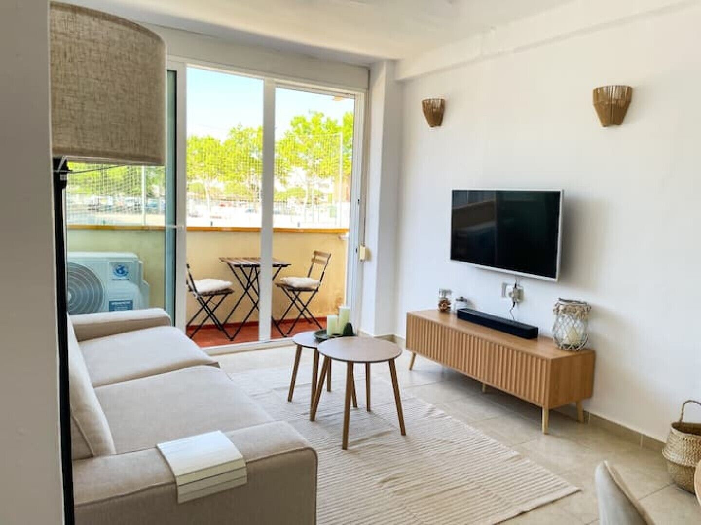 A modern living room with a sofa, a coffee table, a TV, and a balcony with a view of trees.