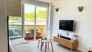 Una sala de estar moderna con un sofá, una mesa de centro, un televisor y un balcón con vistas a árboles.