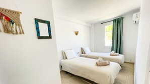 Una habitación con dos camas, una ventana con cortinas, un espejo instalado en la pared y un pequeño adorno mural.