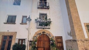 Un edificio con una entrada central en arco, varias ventanas y balcones con plantas en macetas.