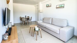 Una sala de estar moderna con sofá, televisor, mesa de comedor, sillas y objetos decorativos.