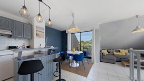 Ett modernt kök med barstolar, en matplats med blå stolar, en grå soffa och utsikt genom glasdörren.