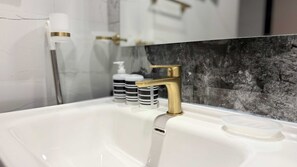 A bathroom with a white sink, a gold faucet, and a marble backsplash. - Skyz Lifestyle 1BR Residences at Arjan (Dubai)
