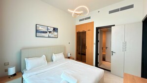 A hotel room with a bed, bedside tables, a wall-mounted artwork, a wardrobe, and a door leading to another room. - Skyz Lifestyle 1BR Residences at Arjan (Dubai)