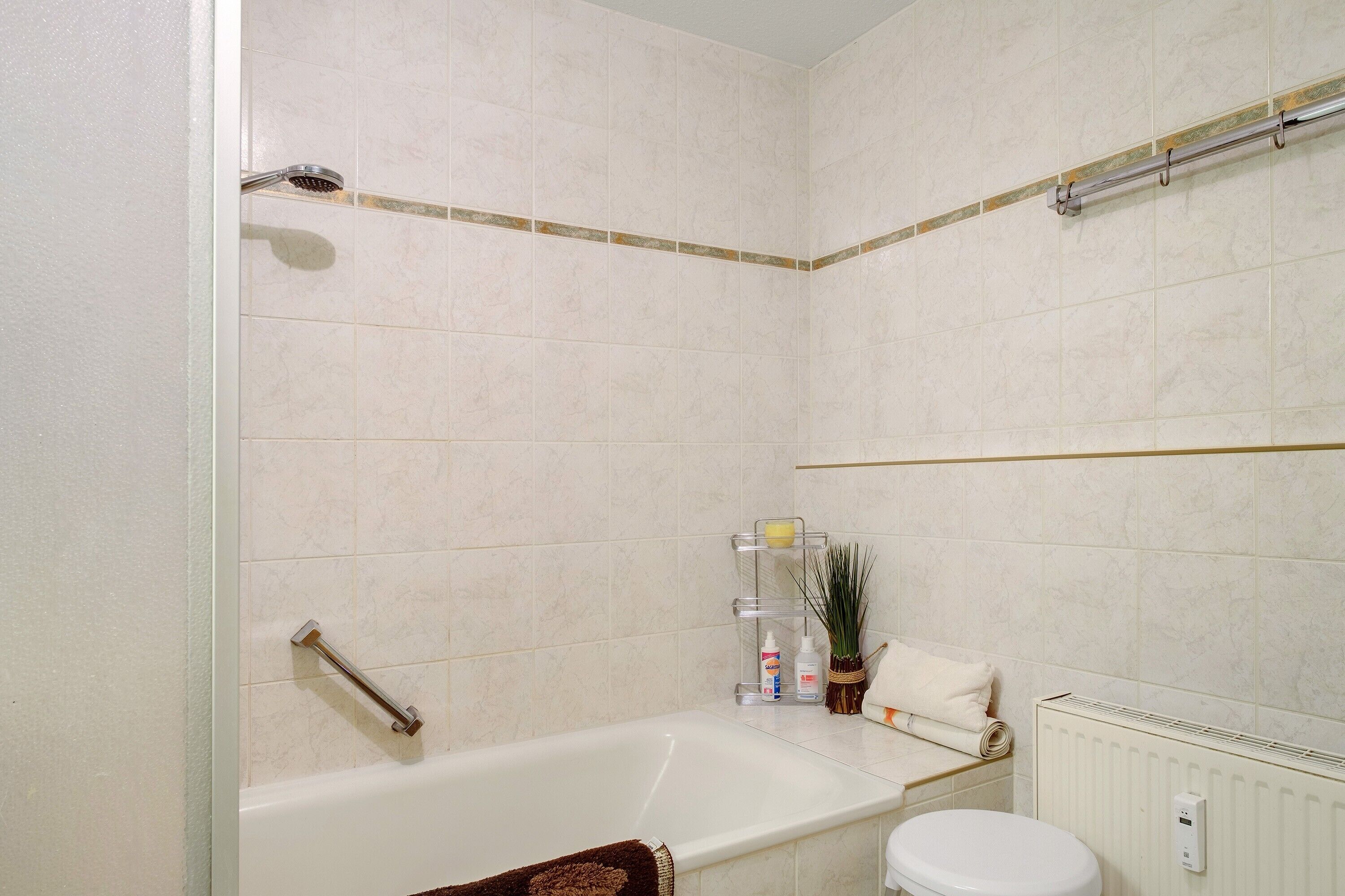 A bathroom with a bathtub, toilet, showerhead, and a towel rack.