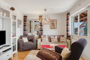 Ein Wohnzimmer mit Fernseher, Sofas, einem roten Tisch und einer Chandelüster.