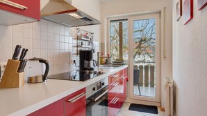 Eine moderne Küche mit roten Schränken, einem Wasserkocher, einer Kaffeemaschine und Blick durch eine Glastür.