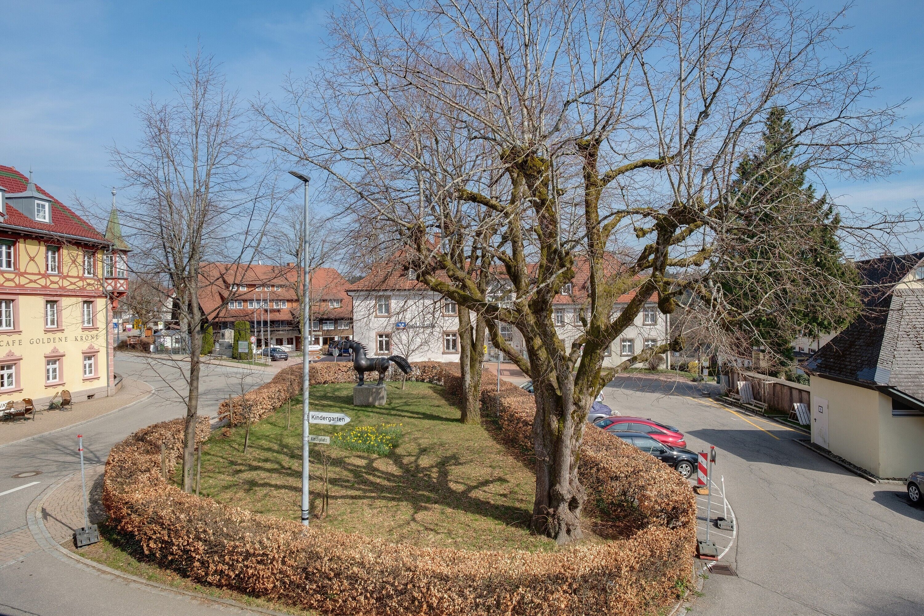 A street view with a café, a kindergarten, and a statue of a horse.