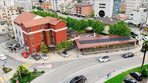A multi-story building with a red facade, a covered outdoor seating area, and a solar panel installation on the roof. - B&B Croce Federale Solduno (Locarno)