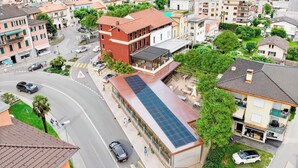 A residential area with a building featuring a solar panel roof, a pedestrian crossing, and a road with cars.