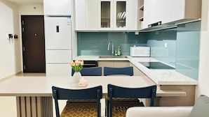A modern kitchen with white cabinets, a built-in microwave, and a dining area with a table and chairs. - SS Home Sunrise City Premium (Ho Chi Minh City)