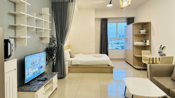 A modern hotel room with a bed, a TV, a desk, and a view of the city. - SS Home Sunrise City Premium (Ho Chi Minh City)