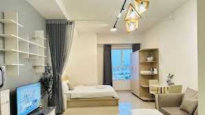A modern hotel room with a bed, a TV, a sofa, a dining table, and a view of the city. - SS Home Sunrise City Premium (Ho Chi Minh City)