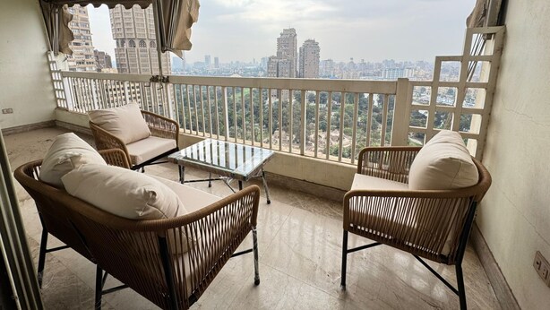 Un balcone con mobili in vimini, un tavolino in vetro e vista sulla città.
