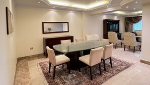Un'ampia sala da pranzo con tavolo in vetro e sedie imbottite, uno specchio grande appeso al muro e una televisione sullo sfondo.