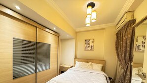 Una camera da letto con un letto grande, pavimento in legno, un lampadario, un comodino e una finestra con persiane.