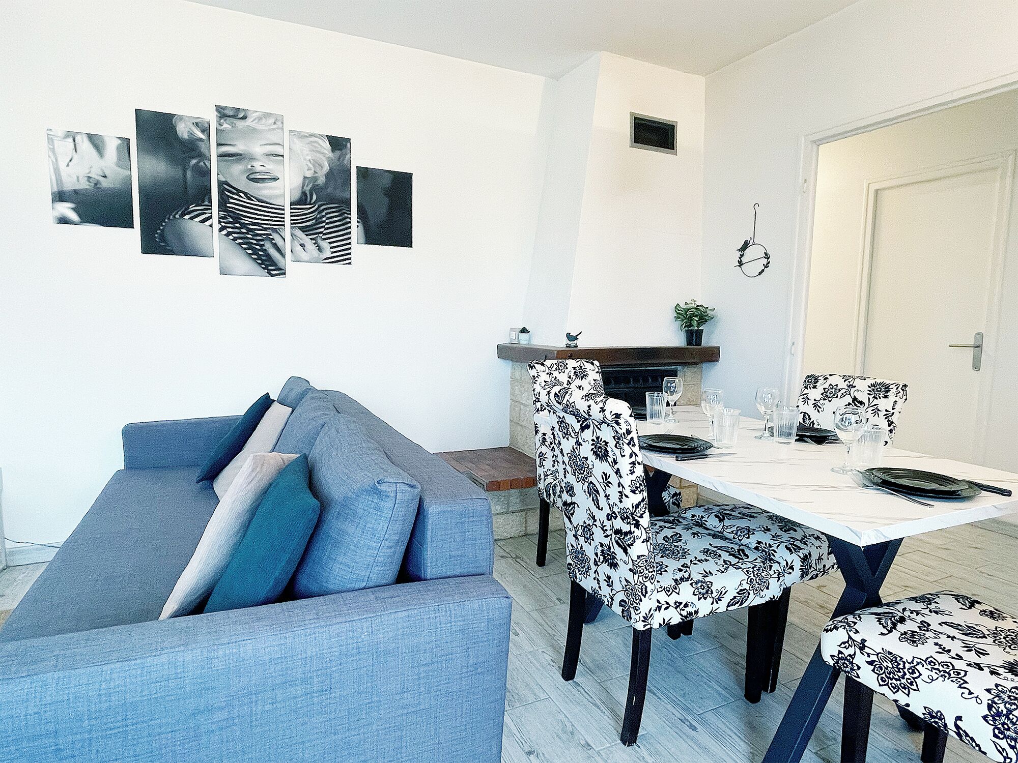 A modern living room with a grey sofa, a dining table set with chairs, and a fireplace.