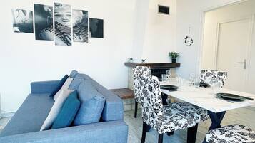A modern living room with a grey sofa, a dining table set with chairs, and a fireplace.