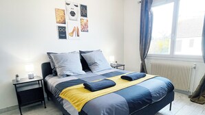 Une chambre à coucher avec un lit, deux tables de chevet, une fenêtre avec des rideaux et des éléments de décoration murale.