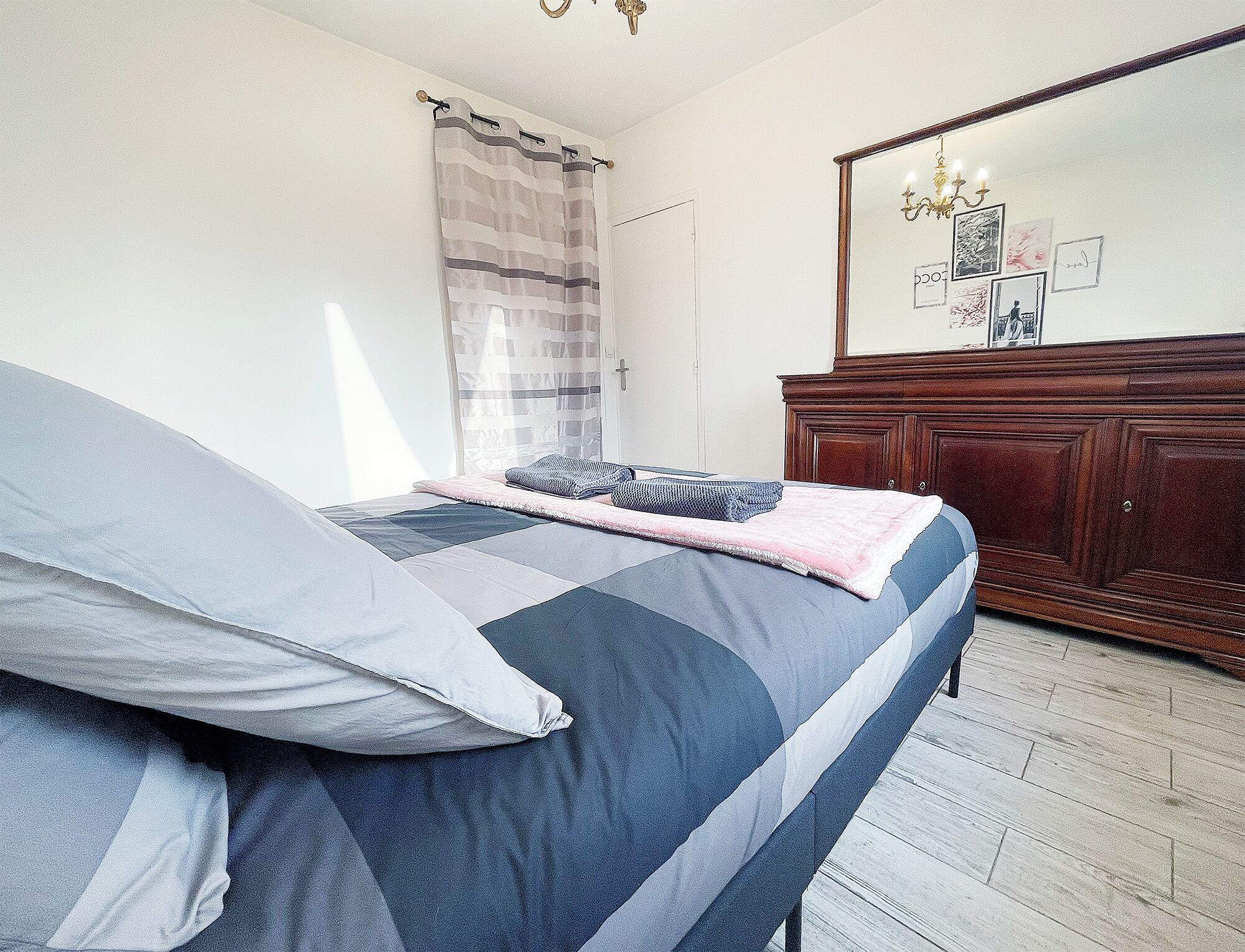 Un dormitorio con cama, cómoda de madera, espejo y ventana con cortinas.