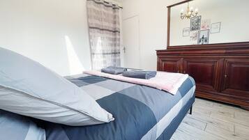 Un dormitorio con cama, cómoda de madera, espejo y ventana con cortinas.