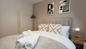 Una cama bien hecha con toallas enrolladas, una lámpara de noche y arte abstracto en la pared.