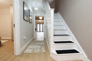 A staircase with white steps and black risers, a hallway with light-colored walls, and a patterned rug on the floor.