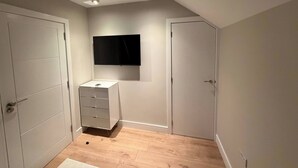 Una habitación con un televisor de pantalla plana en la pared, un tocador blanco y dos puertas.