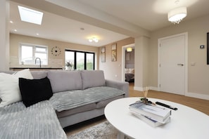 A modern living room with a grey sofa, a round coffee table, and a kitchen in the background. - Modern 5BR Home new (Bristol)